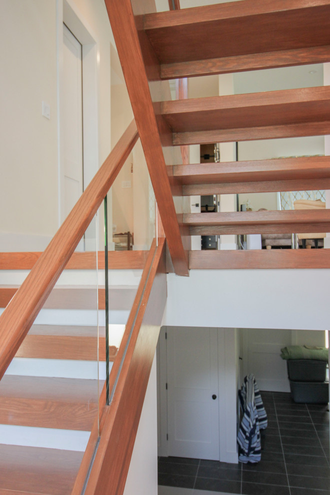 Источник вдохновения для домашнего уюта: лестница на больцах, среднего размера в стиле модернизм с деревянными ступенями, стеклянными перилами и панелями на части стены