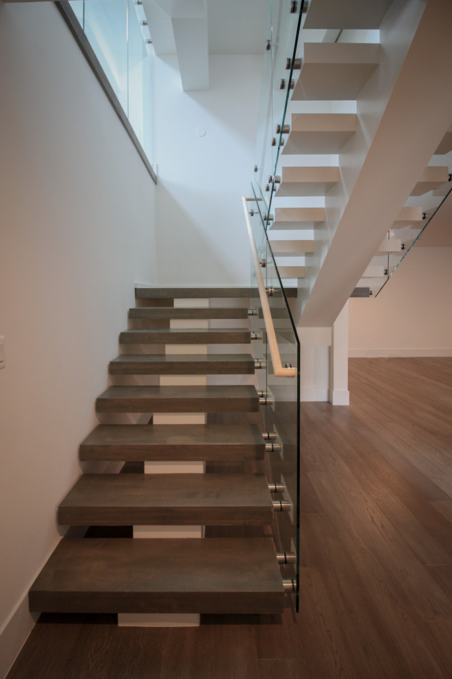 На фото: огромная лестница на больцах в стиле модернизм с деревянными ступенями и стеклянными перилами