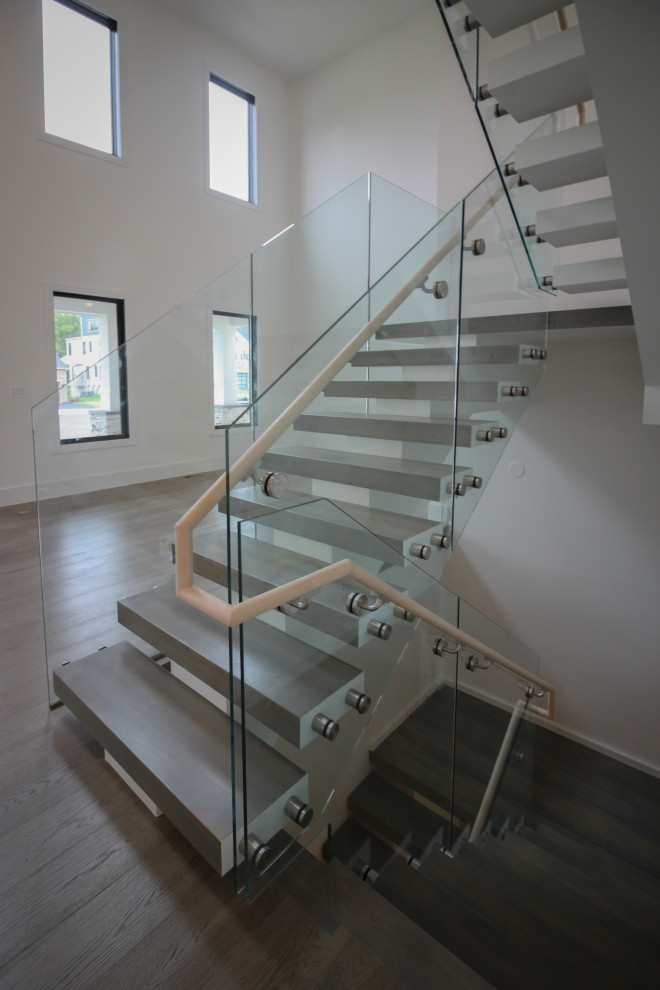 Cette image montre un très grand escalier flottant minimaliste avec des marches en bois et un garde-corps en verre.