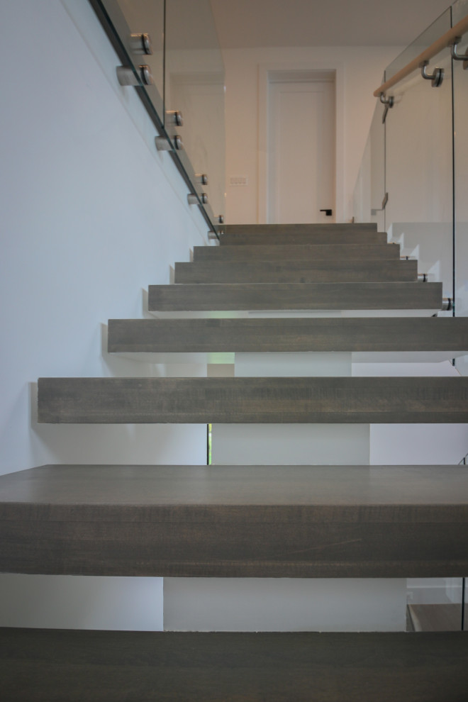 Idée de décoration pour un très grand escalier flottant minimaliste avec des marches en bois et un garde-corps en verre.