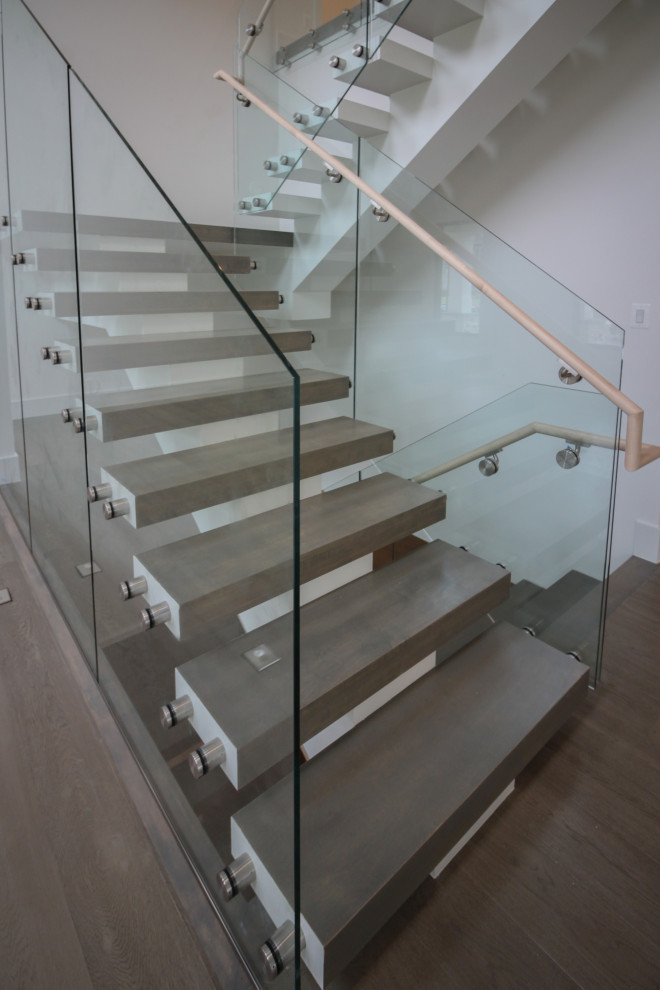 Стильный дизайн: огромная лестница на больцах в стиле модернизм с деревянными ступенями и стеклянными перилами - последний тренд
