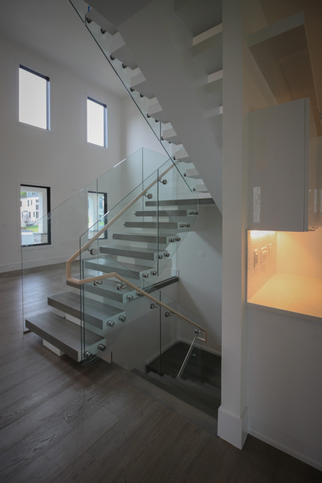 Cette photo montre un très grand escalier flottant moderne avec des marches en bois et un garde-corps en verre.