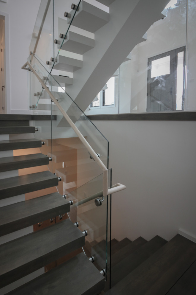 На фото: огромная лестница на больцах в стиле модернизм с деревянными ступенями и стеклянными перилами с