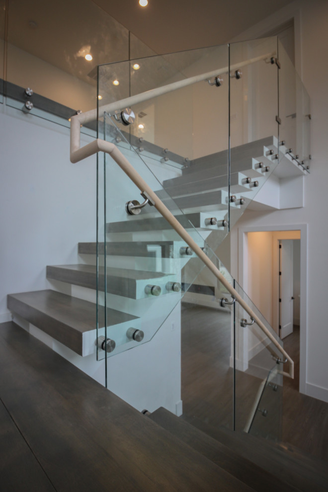 На фото: огромная лестница на больцах в стиле модернизм с деревянными ступенями и стеклянными перилами с