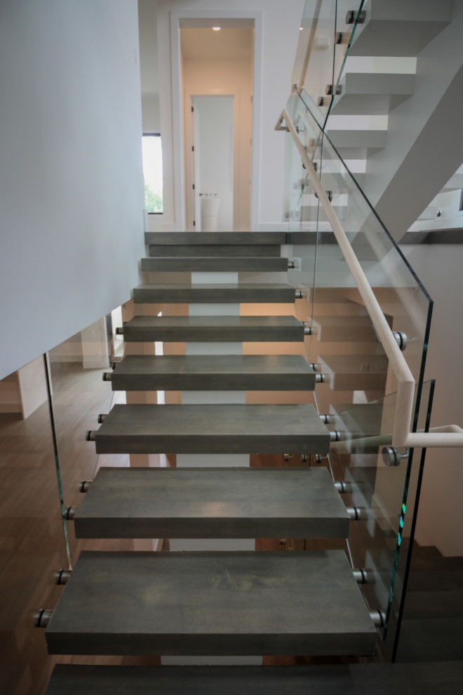 Aménagement d'un très grand escalier flottant moderne avec des marches en bois et un garde-corps en verre.