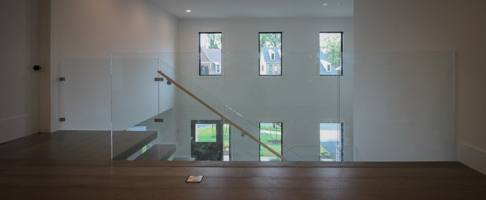 Cette image montre un très grand escalier flottant minimaliste avec des marches en bois et un garde-corps en verre.