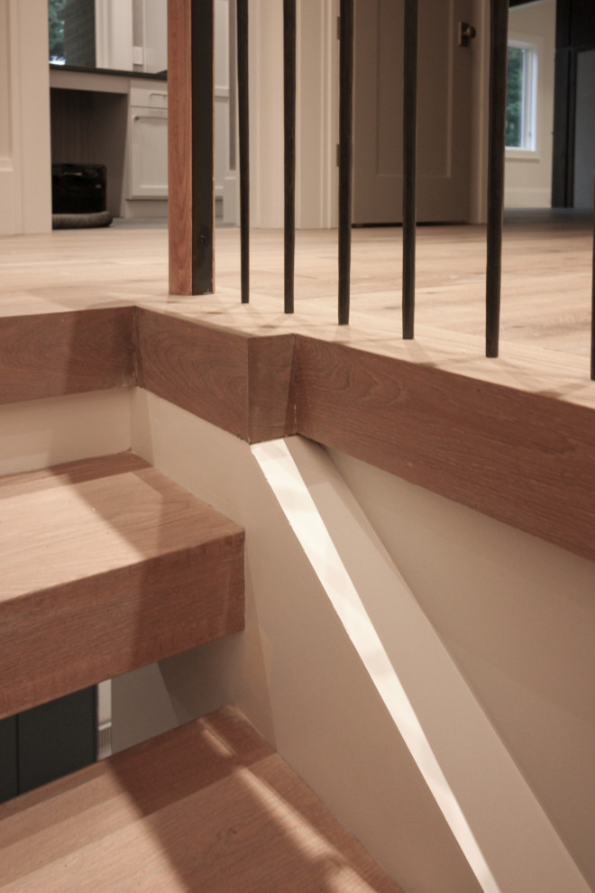 Cette image montre un grand escalier minimaliste en U avec des marches en bois, des contremarches en bois, un garde-corps en métal et du papier peint.