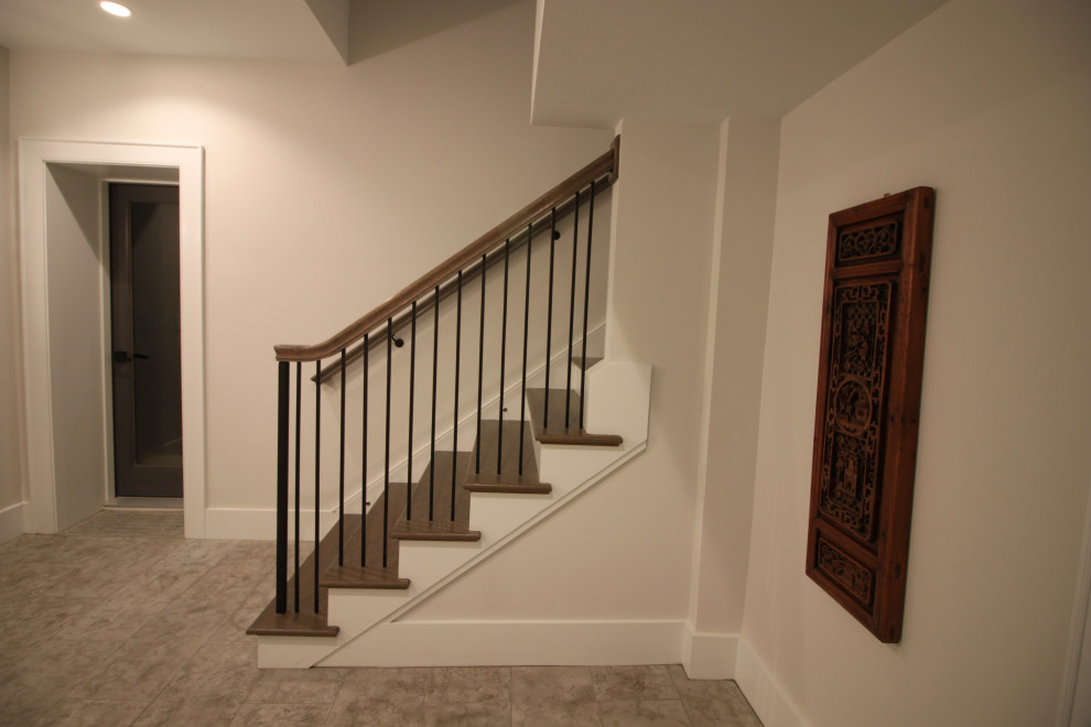 Стильный дизайн: большая угловая лестница в стиле неоклассика (современная классика) с деревянными ступенями, крашенными деревянными подступенками, металлическими перилами и панелями на части стены - последний тренд