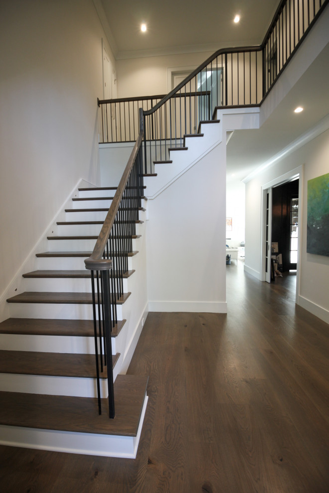 Large traditional wood l-shaped metal railing staircase in DC Metro with painted wood risers and panelled walls.