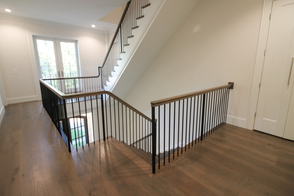 Aménagement d'un grand escalier peint classique en L avec des marches en bois, un garde-corps en métal et du lambris.