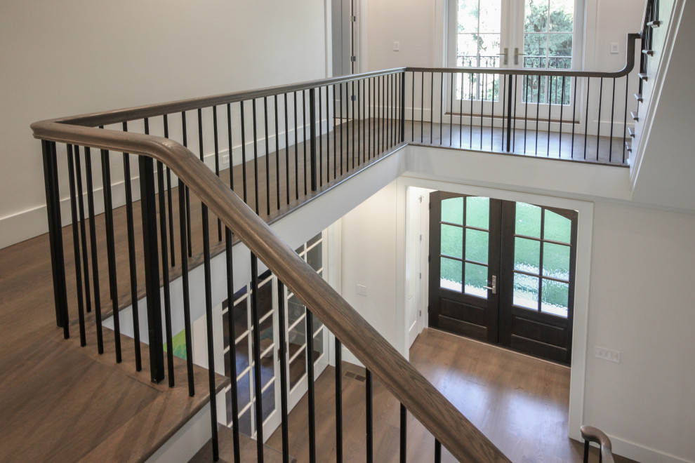 Идея дизайна: большая угловая лестница в стиле неоклассика (современная классика) с деревянными ступенями, крашенными деревянными подступенками, металлическими перилами и панелями на части стены
