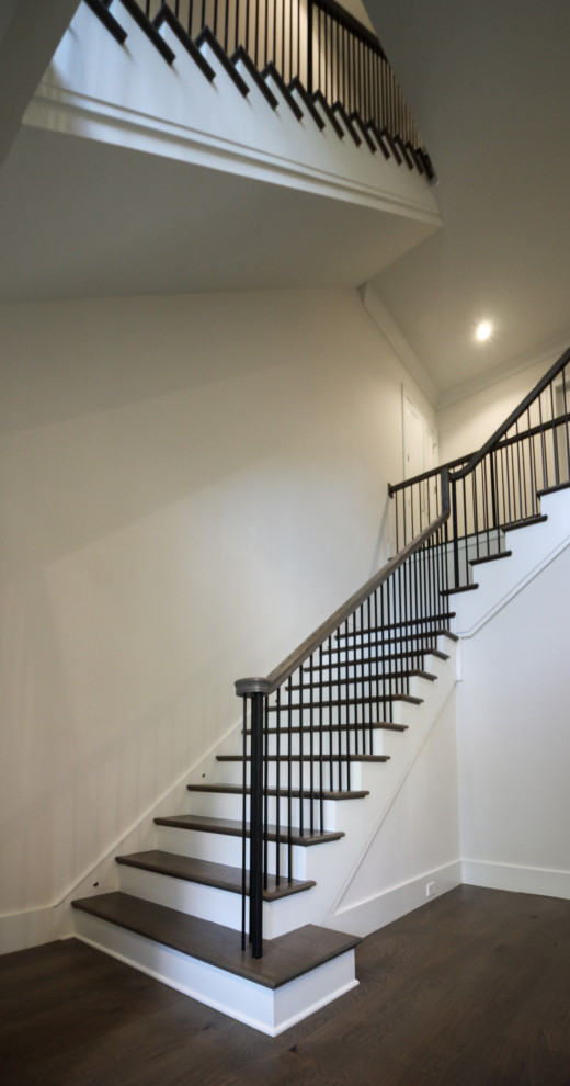 На фото: большая угловая лестница в стиле неоклассика (современная классика) с деревянными ступенями, крашенными деревянными подступенками, металлическими перилами и панелями на части стены