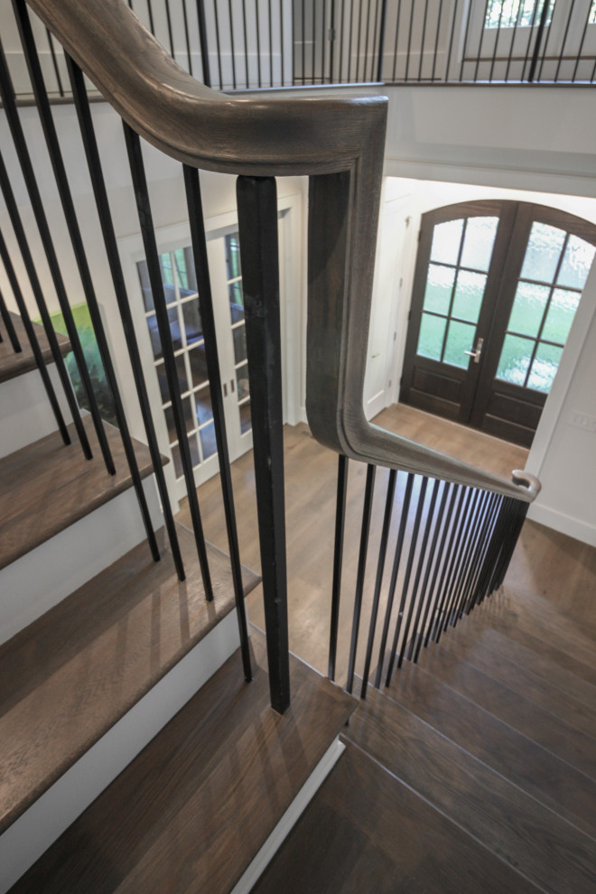 Идея дизайна: большая угловая лестница в стиле неоклассика (современная классика) с деревянными ступенями, крашенными деревянными подступенками, металлическими перилами и панелями на части стены