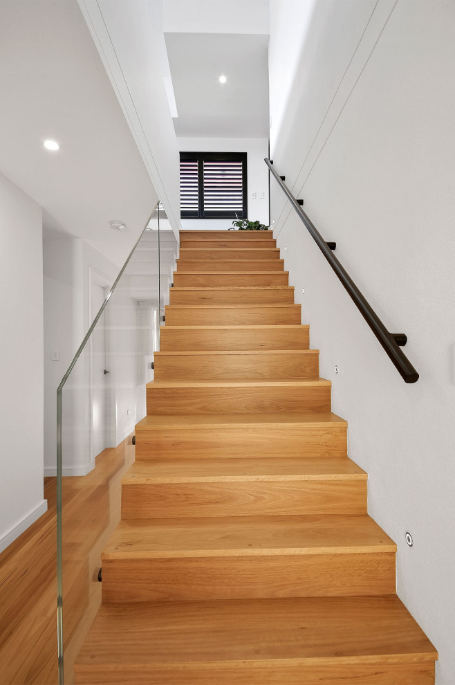 Пример оригинального дизайна: большая прямая лестница в современном стиле с деревянными ступенями, стеклянными подступенками и металлическими перилами