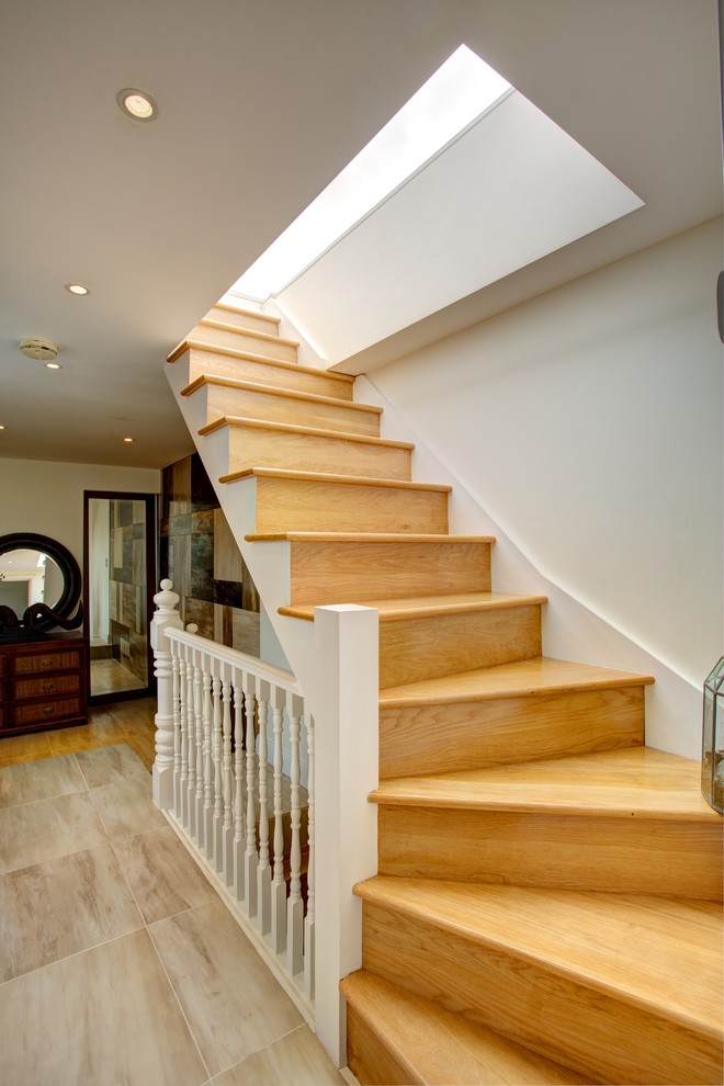 This is an example of a contemporary wood curved staircase in London with wood risers and feature lighting.