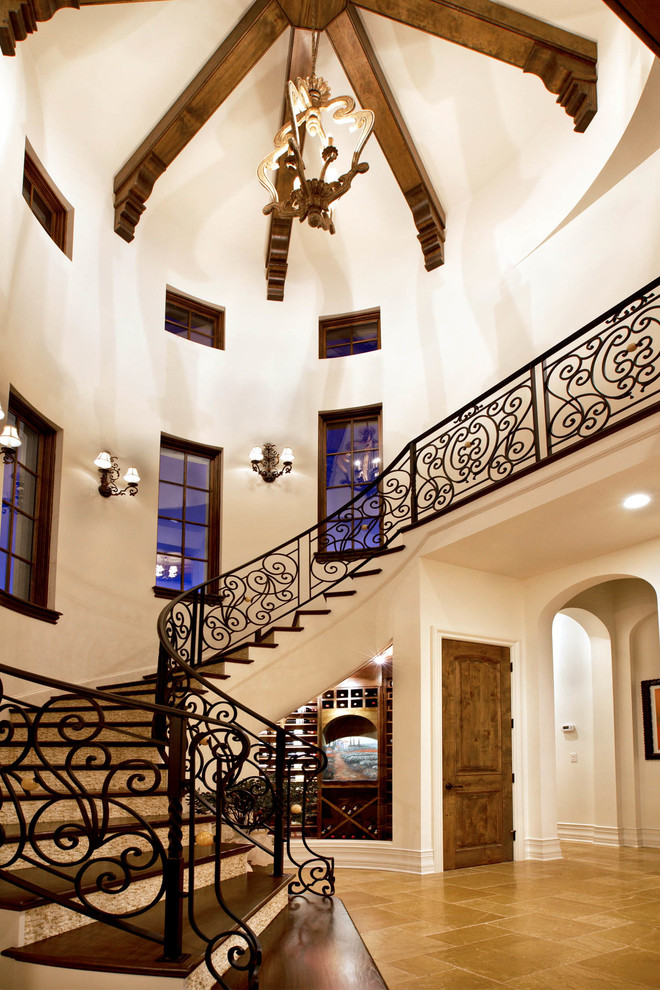 Идея дизайна: большая изогнутая лестница в средиземноморском стиле с деревянными ступенями, крашенными деревянными подступенками и металлическими перилами