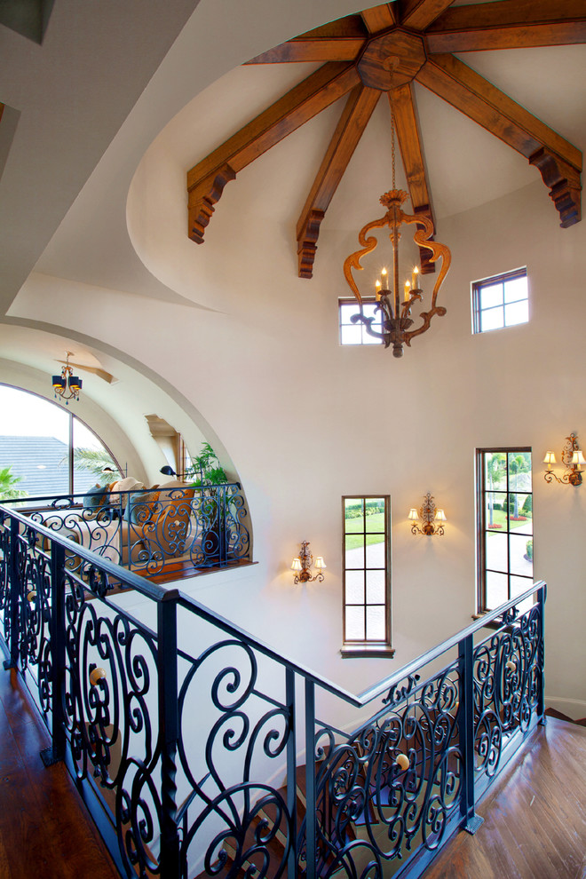 На фото: большая изогнутая лестница в средиземноморском стиле с деревянными ступенями, крашенными деревянными подступенками и металлическими перилами