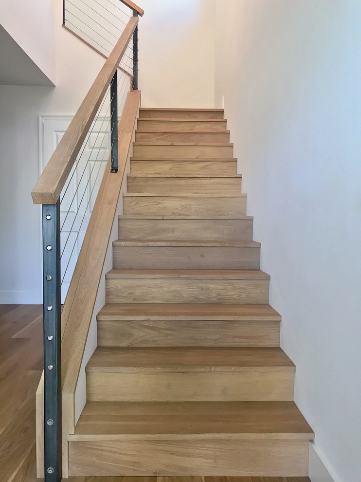 Cette image montre un escalier minimaliste en L de taille moyenne avec des marches en bois, des contremarches en bois et un garde-corps en métal.