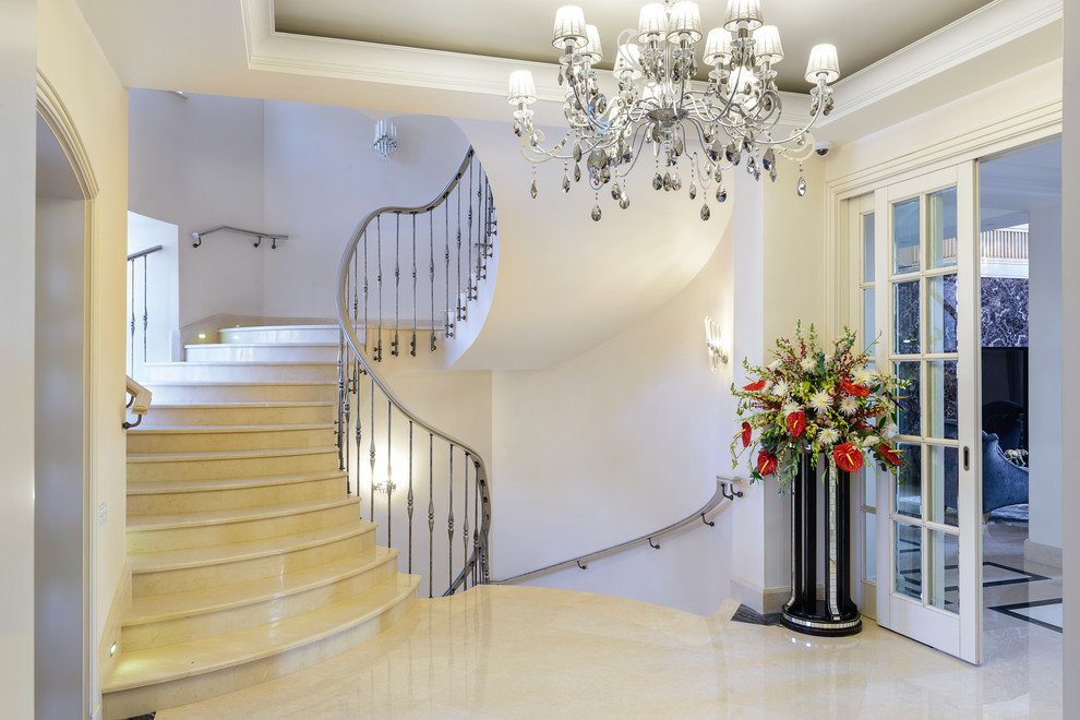 Стильный дизайн: изогнутая лестница в классическом стиле с мраморными ступенями, подступенками из мрамора и металлическими перилами - последний тренд