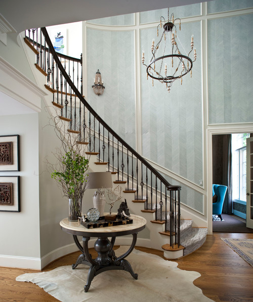 Foyer with round table and wood floor and curved staircase with panels filled with blue striped wallpaper