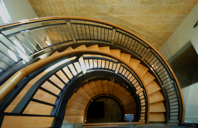 На фото: огромная изогнутая деревянная лестница в стиле неоклассика (современная классика) с деревянными ступенями и металлическими перилами с