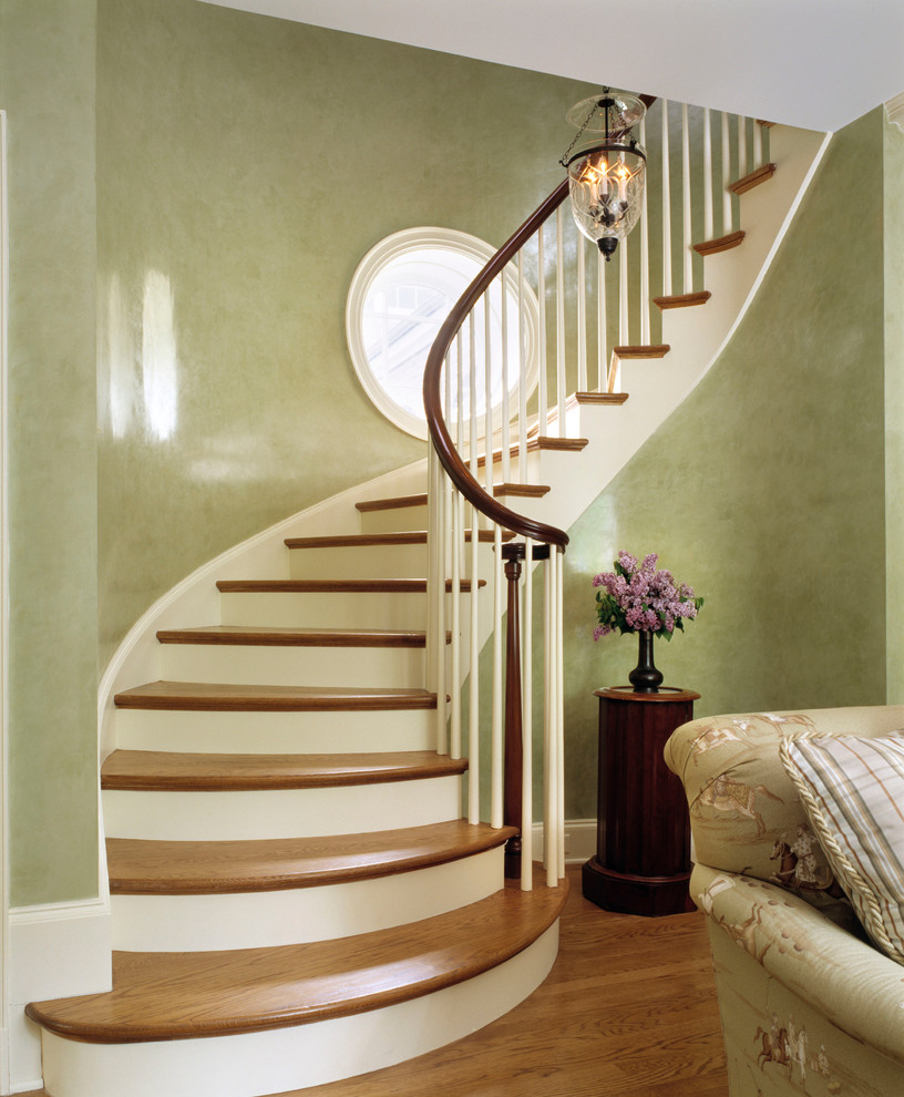 Пример оригинального дизайна: изогнутая лестница в классическом стиле с деревянными ступенями и крашенными деревянными подступенками