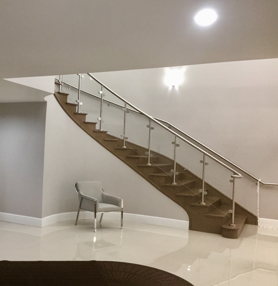 Example of a huge trendy wooden curved glass railing staircase design in Other with wooden risers