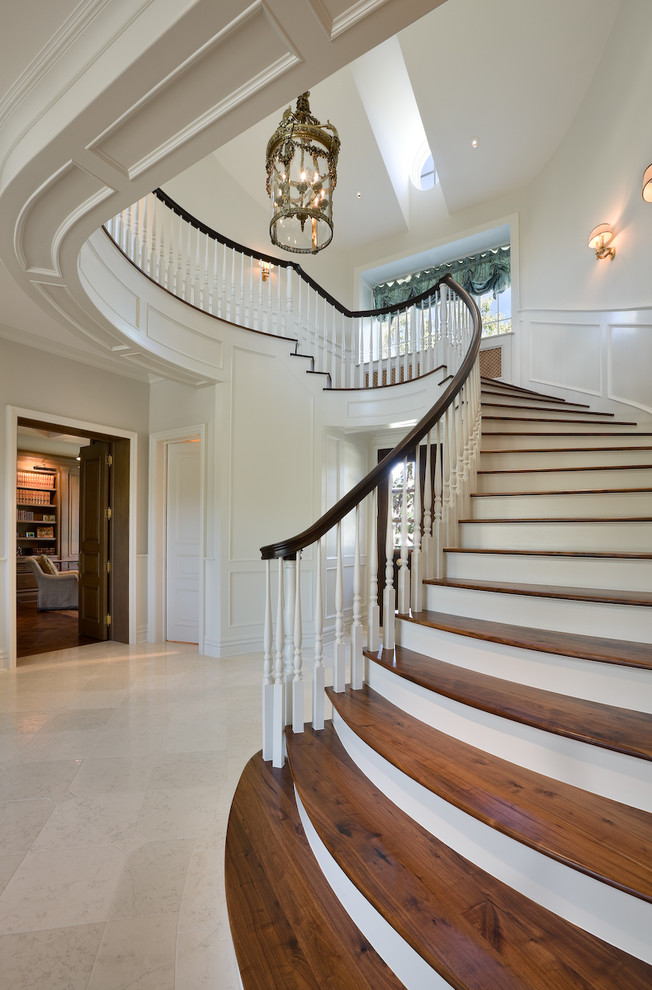 Пример оригинального дизайна: изогнутая лестница в классическом стиле с деревянными ступенями, крашенными деревянными подступенками и деревянными перилами