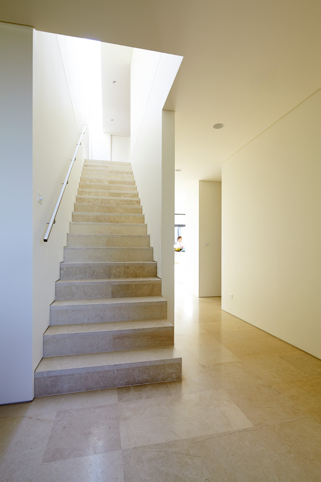 Стильный дизайн: прямая лестница в современном стиле с ступенями из известняка, подступенками из известняка и металлическими перилами - последний тренд