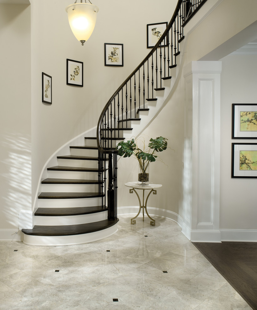 На фото: изогнутая лестница в классическом стиле с деревянными ступенями, крашенными деревянными подступенками и металлическими перилами