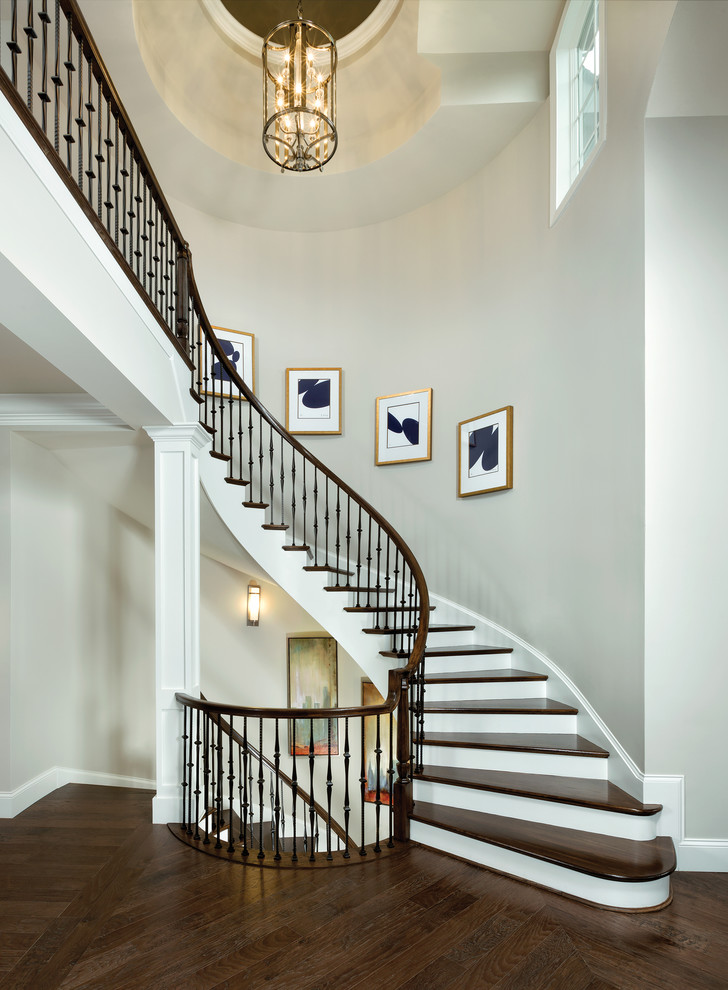 Пример оригинального дизайна: изогнутая лестница в стиле неоклассика (современная классика) с деревянными ступенями и крашенными деревянными подступенками