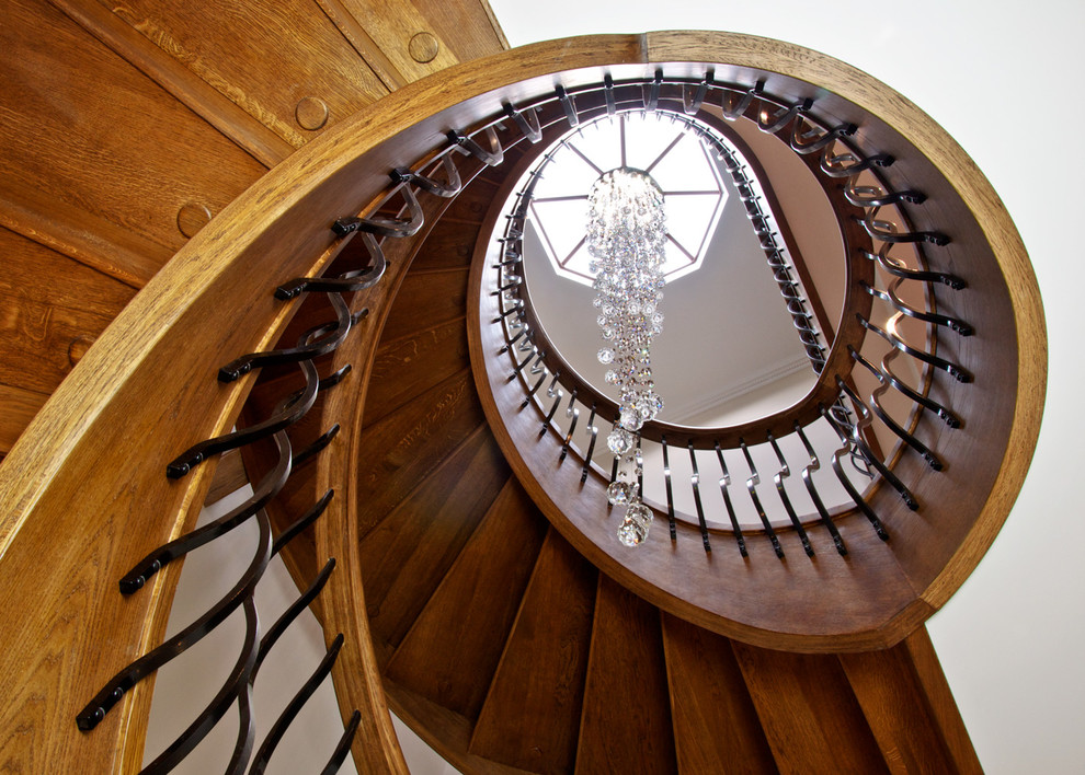 Ejemplo de escalera curva clásica renovada grande con escalones de madera, contrahuellas de madera y barandilla de metal