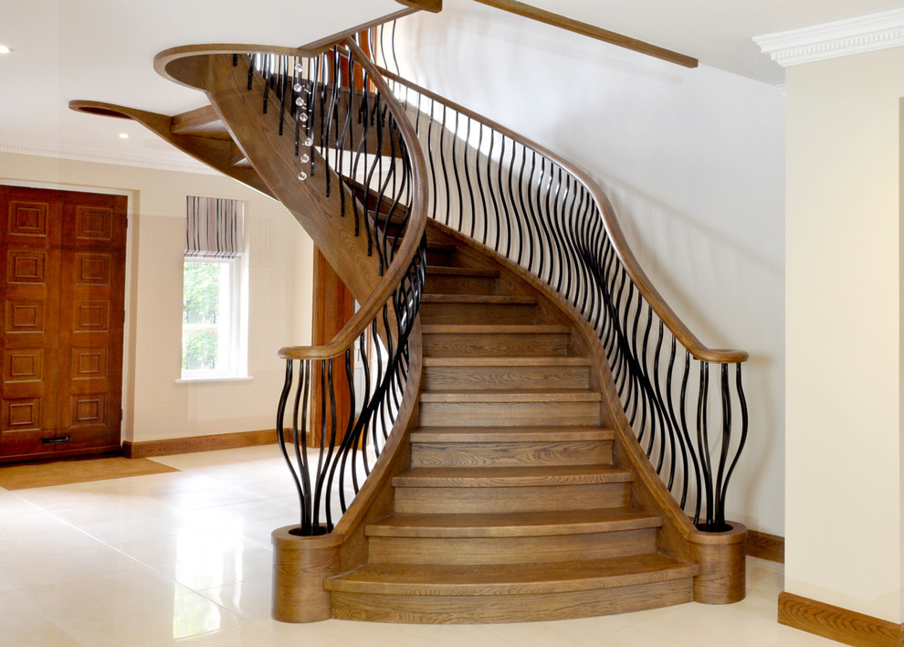 Пример оригинального дизайна: большая изогнутая деревянная лестница в стиле неоклассика (современная классика) с деревянными ступенями и металлическими перилами