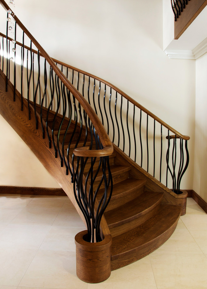 Свежая идея для дизайна: большая изогнутая деревянная лестница в стиле неоклассика (современная классика) с деревянными ступенями и металлическими перилами - отличное фото интерьера