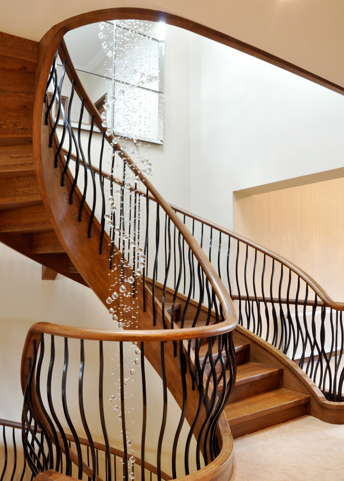 Стильный дизайн: большая изогнутая деревянная лестница в стиле неоклассика (современная классика) с деревянными ступенями и металлическими перилами - последний тренд