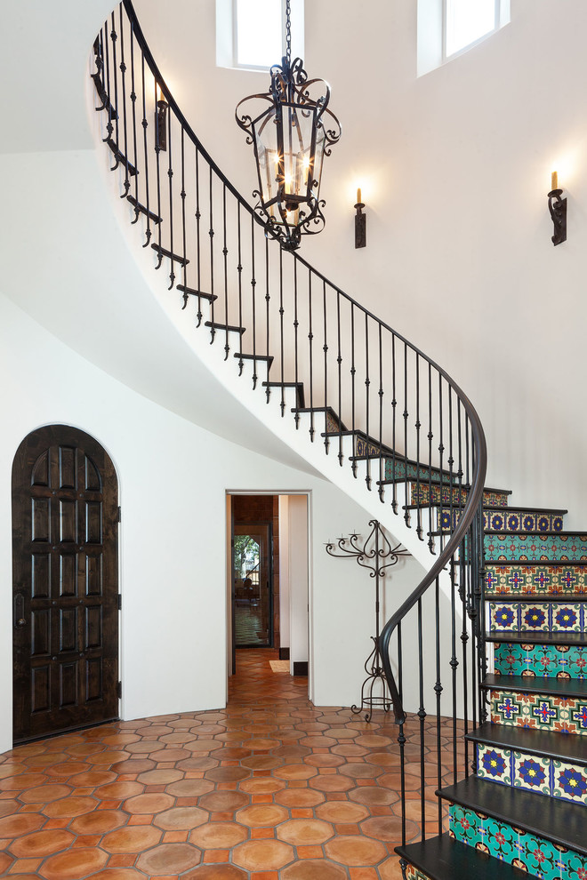 Пример оригинального дизайна: изогнутая лестница в средиземноморском стиле с подступенками из плитки и металлическими перилами