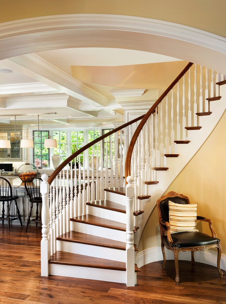 Пример оригинального дизайна: огромная изогнутая лестница в классическом стиле с деревянными ступенями и крашенными деревянными подступенками