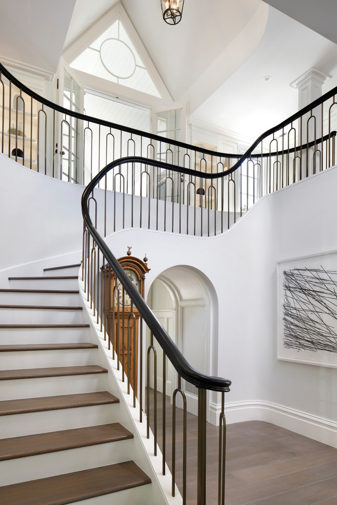 Ejemplo de escalera curva tradicional con escalones de madera, contrahuellas de madera pintada y barandilla de metal