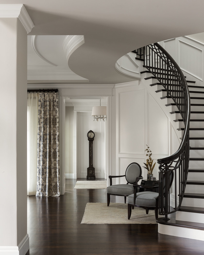 Пример оригинального дизайна: большая изогнутая лестница в классическом стиле с деревянными ступенями, крашенными деревянными подступенками и металлическими перилами
