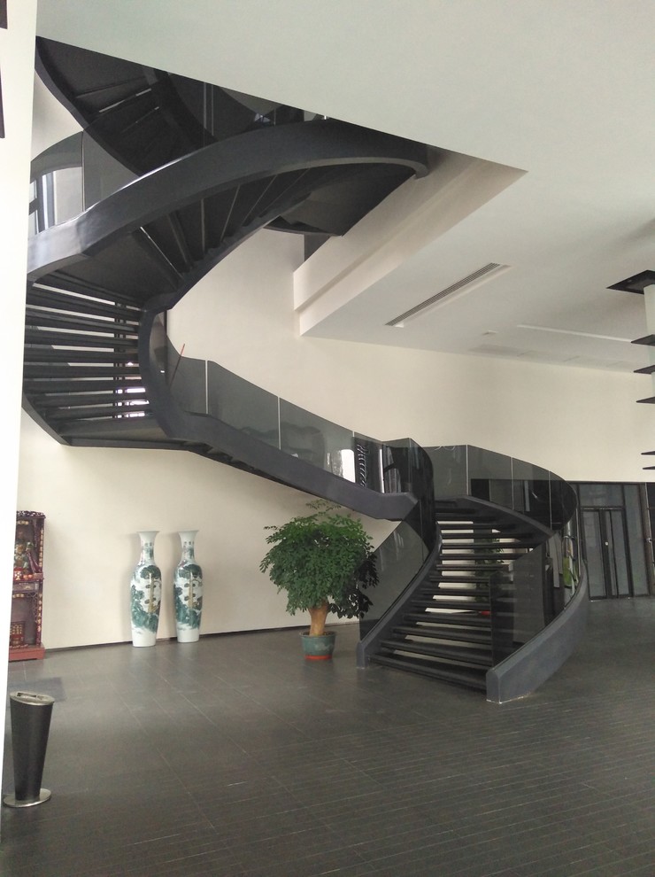 На фото: большая изогнутая лестница в стиле модернизм с ступенями из плитки и стеклянными перилами без подступенок