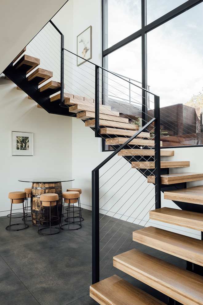 На фото: лестница на больцах в стиле модернизм с деревянными ступенями и перилами из тросов без подступенок