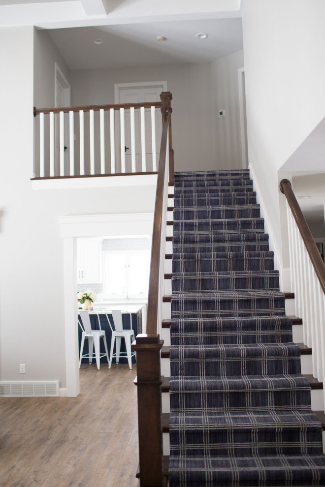 他の地域にある高級な広いトランジショナルスタイルのおしゃれな直階段 (カーペット張りの蹴込み板、木材の手すり) の写真