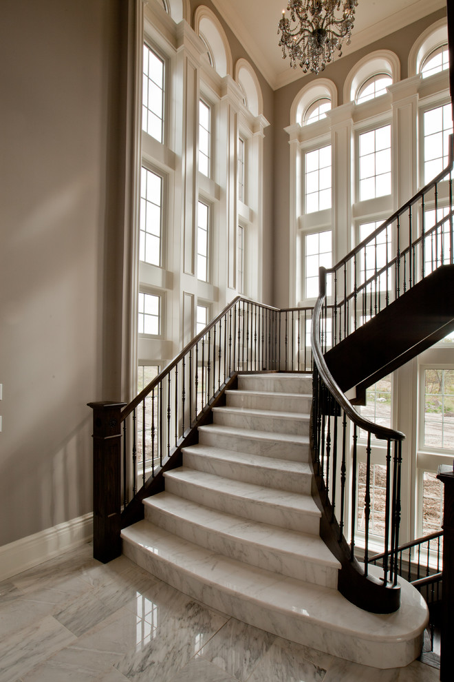 На фото: огромная изогнутая лестница в классическом стиле с металлическими перилами, мраморными ступенями и подступенками из мрамора с