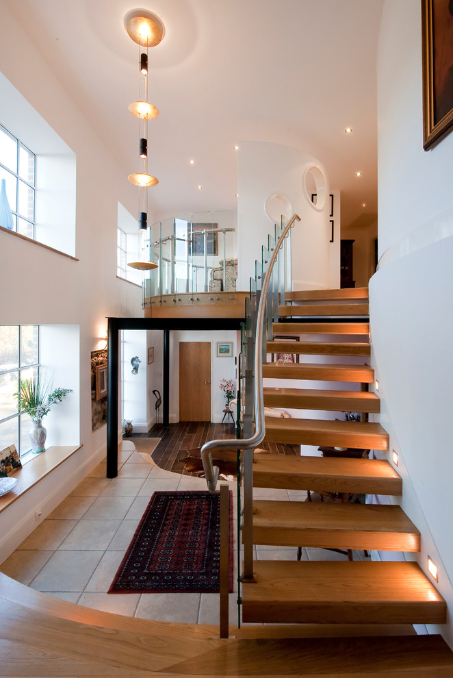 Свежая идея для дизайна: изогнутая лестница в современном стиле с деревянными ступенями и стеклянными перилами без подступенок - отличное фото интерьера