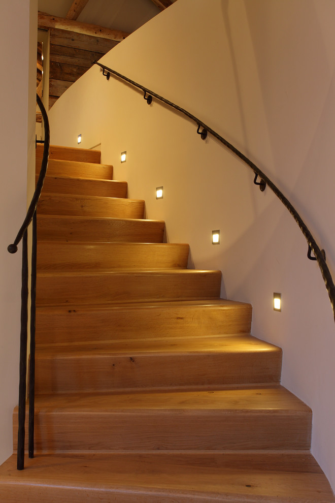 Cette image montre un escalier courbe minimaliste avec des marches en bois, des contremarches en bois et éclairage.