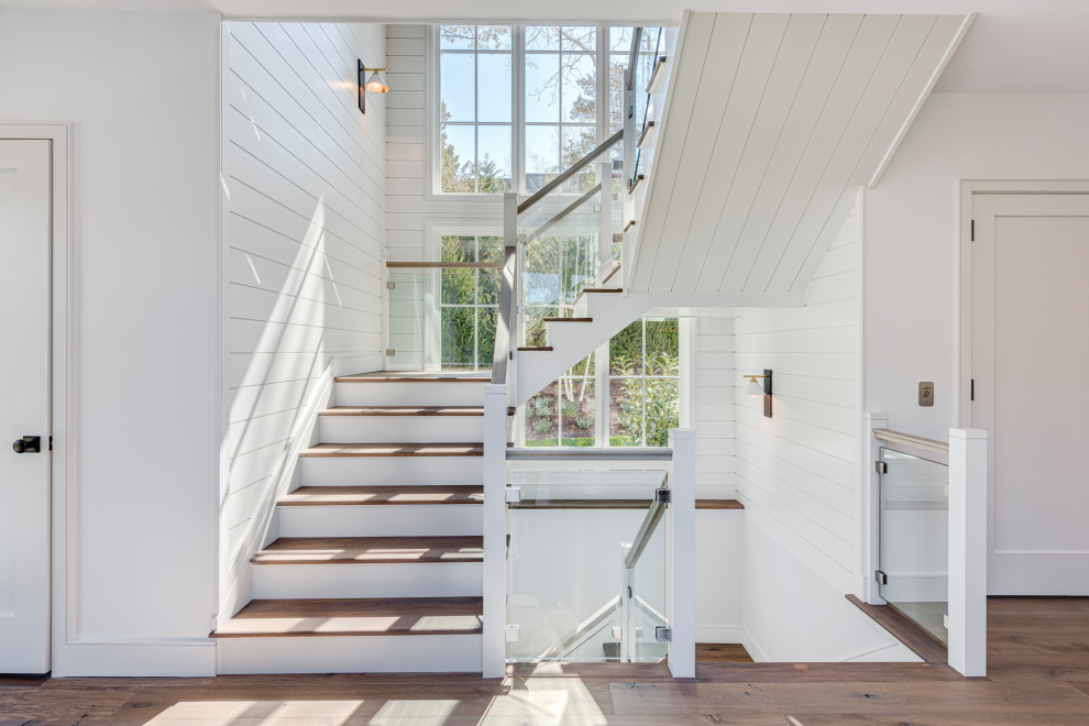 На фото: п-образная деревянная лестница в морском стиле с стеклянными перилами и деревянными стенами с