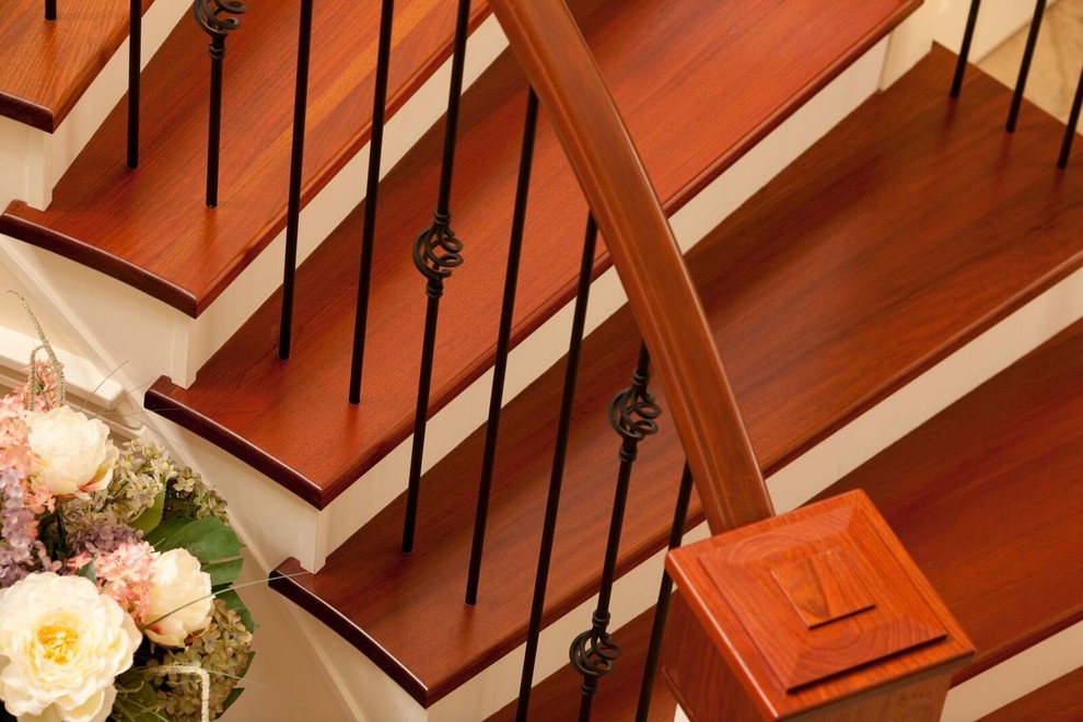 Стильный дизайн: большая изогнутая лестница в классическом стиле с деревянными ступенями, крашенными деревянными подступенками и металлическими перилами - последний тренд