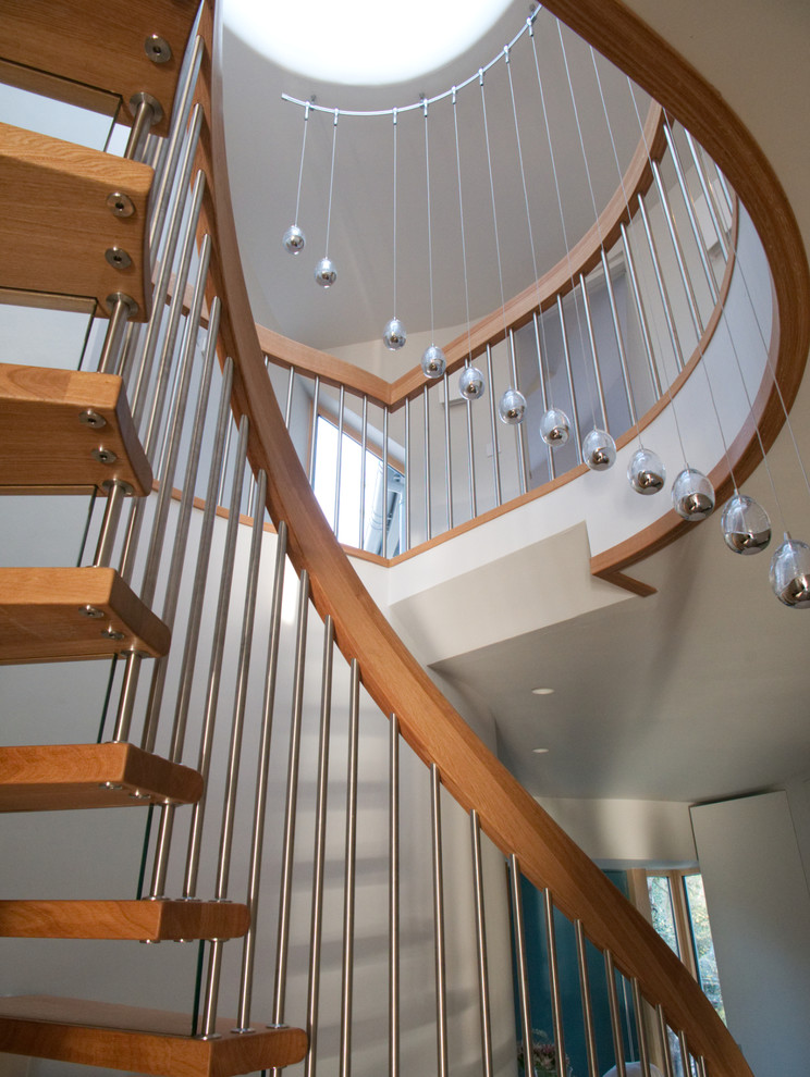 На фото: изогнутая лестница среднего размера в современном стиле с деревянными ступенями, стеклянными подступенками и металлическими перилами