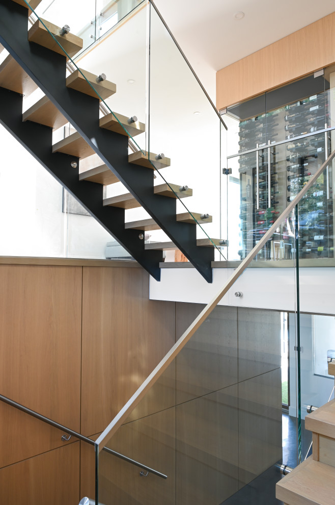 This is an example of a contemporary wood floating glass railing staircase in Vancouver with open risers and wood walls.