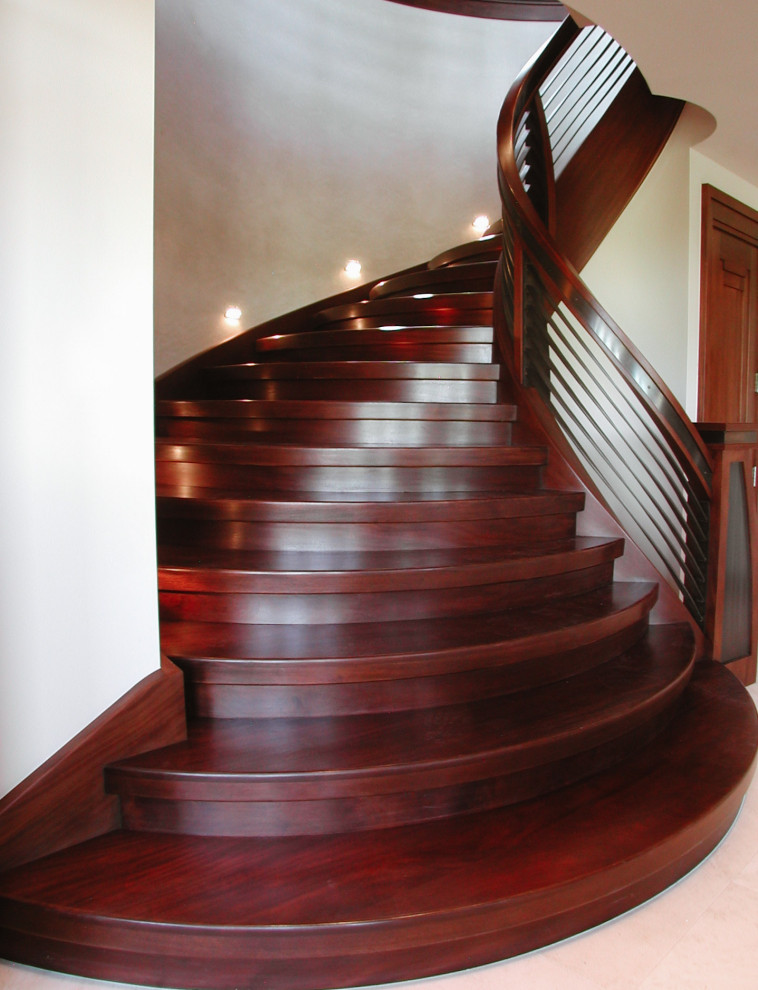 Imagen de escalera curva grande con escalones de madera, contrahuellas de madera y barandilla de varios materiales
